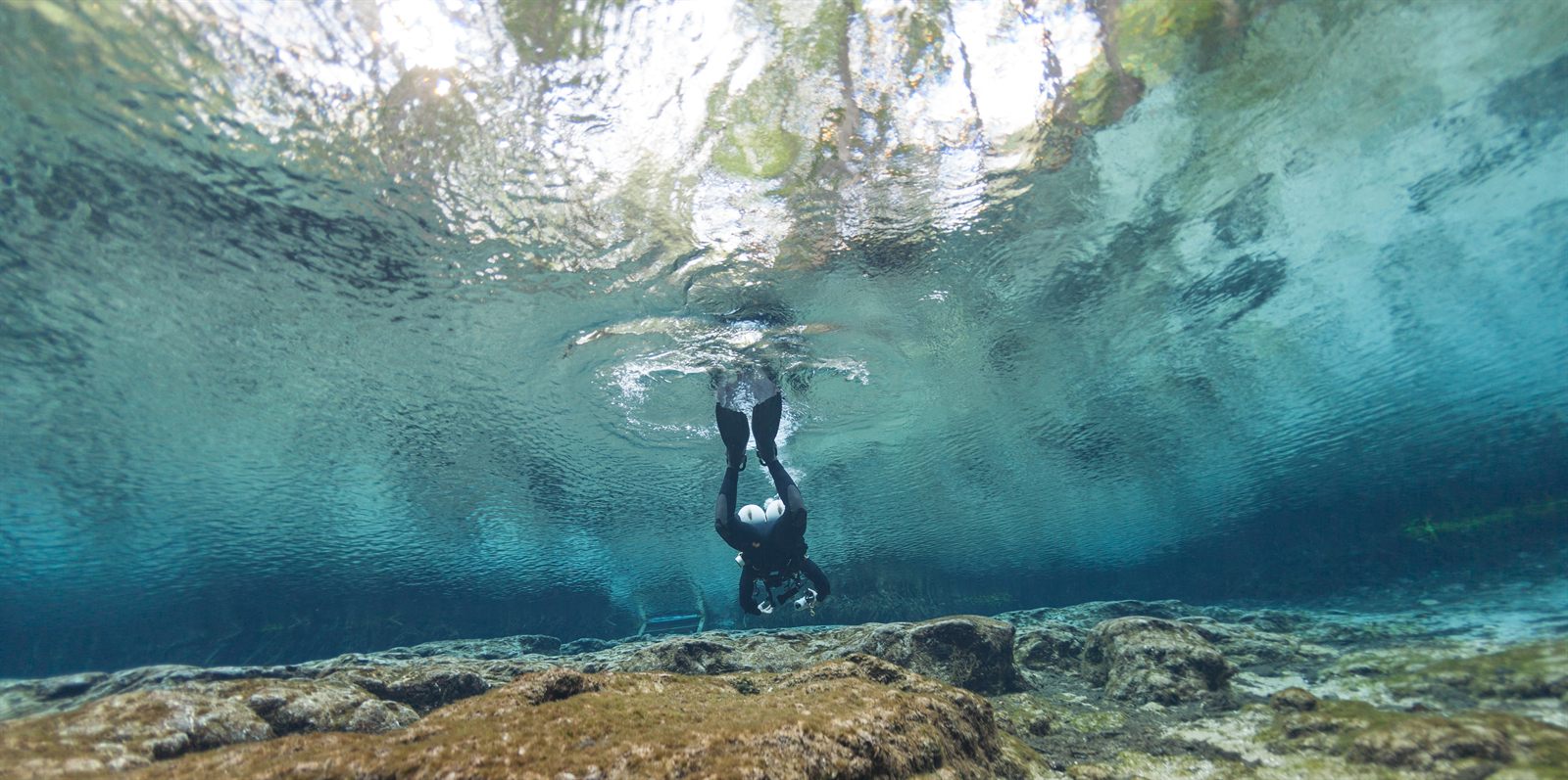 A diver descending through clear blue spring water toward a limestone cave opening at Ginnie Springs